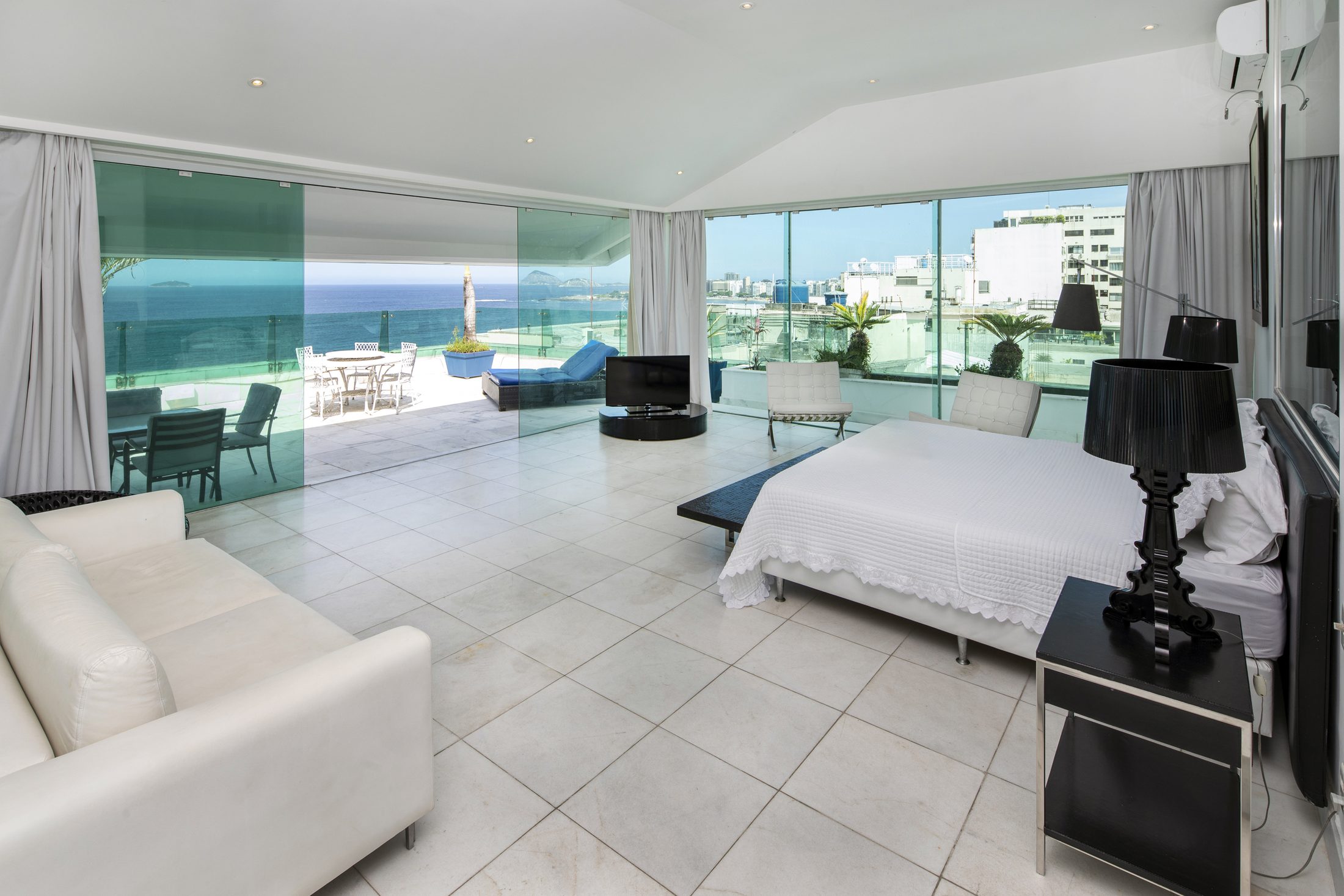 A suite with a king bed and a glass wall opening onto the terrace and the sea
